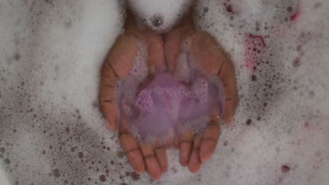 Hands-of-african-american-attractive-woman-taking-bath-with-foam,-salt-and-rose-petals