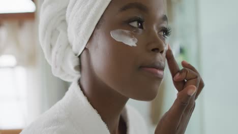 Retrato-De-Una-Mujer-Atractiva-Afroamericana-Aplicando-Crema-Facial-En-El-Baño
