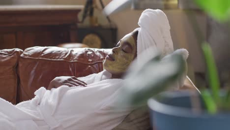 Afroamerikanische-Attraktive-Frau-Mit-Aufgesetzter-Gesichtsmaske,-Die-Auf-Dem-Sofa-Liegt-Und-Sich-Zu-Hause-Entspannt