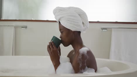 Profile-of-african-american-attractive-woman-relaxing-in-foam-bath-and-drinking-coffee-in-bathroom