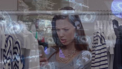Animation-of-data-processing-over-woman-using-smartphone-while-looking-at-clothes-hanging-in-shop