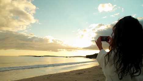 Brunette-taking-a-photo-of-the-sunset-on-her-smartphone