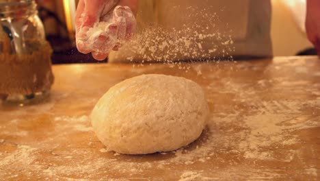 Female-hand-sprinkling-flour-on-ball-of-dough-on-a-floury-surface