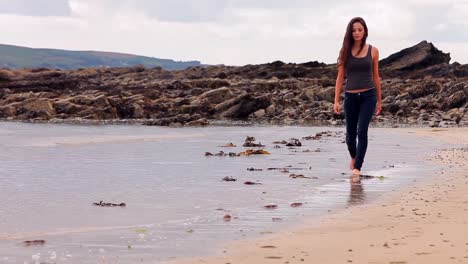 Pretty-brunette-walking-along-the-water-by-the-beach