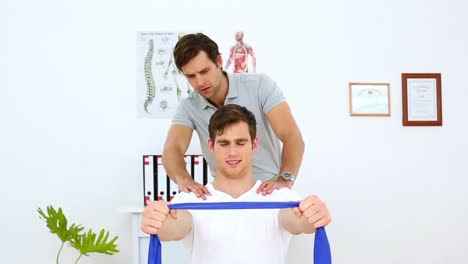 Physiotherapist-checking-shoulder-alignment-of-patient-pulling-resistance-band