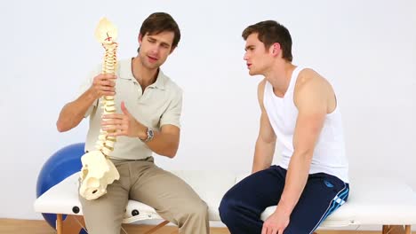 Physiotherapist-speaking-to-patient-showing-him-a-spine-model