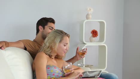 Paar-Liegt-Auf-Der-Couch-Und-Benutzt-Einen-Tablet-PC,-Der-Wein-Trinkt