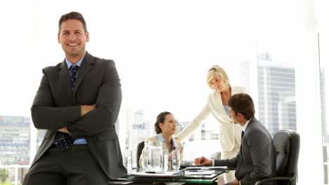 Businessman-leaning-on-desk-with-team-behind-him
