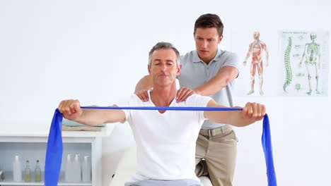 Physiotherapist-checking-mature-patient-stretching-resistance-band