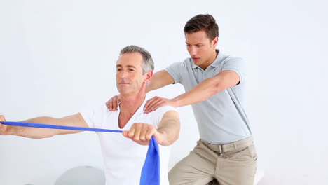 Physiotherapist-checking-senior-patient-stretching-blue-resistance-band