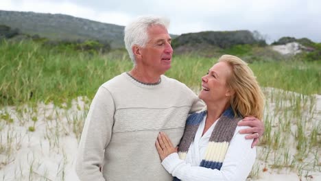 Smiling-retired-couple-standing-on-the-beach
