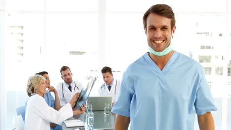 Surgeon-taking-off-mask-with-staff-talking-behind-him-