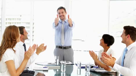 Businessman-receiving-praise-from-his-employees-at-meeting-and-giving-thumbs-up