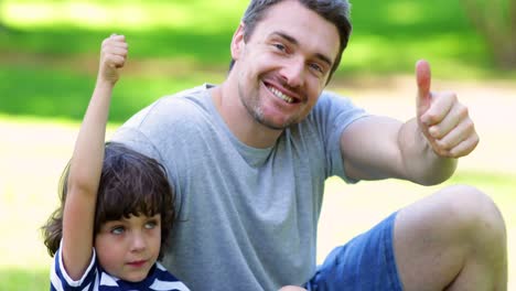 Father-sitting-with-little-son-in-the-park-showing-thumbs-up