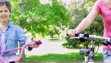 Cute-mother-and-daughter-pushing-their-bikes-together-in-the-park