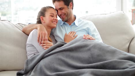 Cute-couple-lying-on-couch-chatting-under-a-blanket
