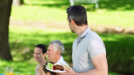 Happy-father-offering-plate-of-food-to-camera-at-family-barbecue