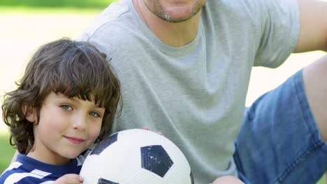 Father-sitting-with-little-son-holding-football-in-the-park
