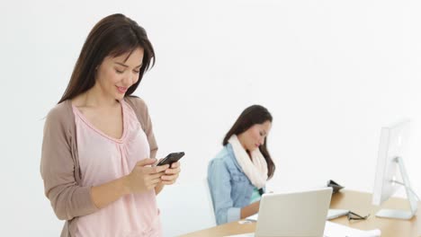 Creative-businesswoman-sending-a-text-with-colleague-behind-her