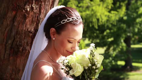 Hübsche-Braut-Hält-Einen-Blumenstrauß-Im-Park-Und-Lächelt-In-Die-Kamera
