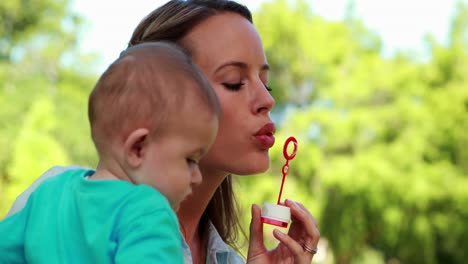 Glückliche-Mutter-Bläst-Seifenblasen-Mit-Süßem-Kleinen-Sohn-Im-Park