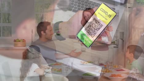 Man-holding-a-smartphone-with-qr-code-on-screen-against-caucasian-family-having-lunch-together