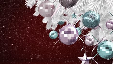 Snow-falling-over-bauble-and-star-decorations-hanging-on-christmas-tree-against-red-background