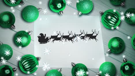 Snowflakes-over-santa-claus-in-sleigh-being-pulled-by-reindeers-on-paper-and-multiple-green-baubles