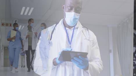 Composite-of-male-doctor-in-face-mask-using-tablet,-and-diverse-doctors-in-masks-walking-in-corridor