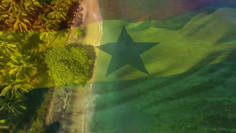Digital-composition-of-waving-ghana-flag-against-aerial-view-of-the-beach-and-sea-waves