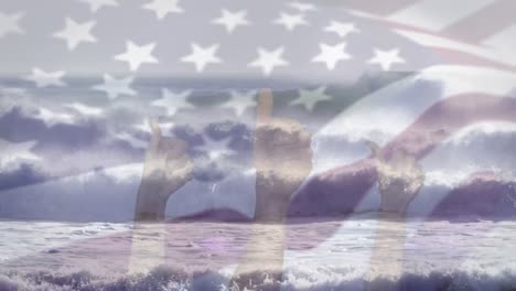Digitale-Komposition-Der-Schwenkenden-US-Flagge-über-Händen,-Die-Daumen-Nach-Oben-Gegen-Die-Wellen-Im-Meer-Zeigen