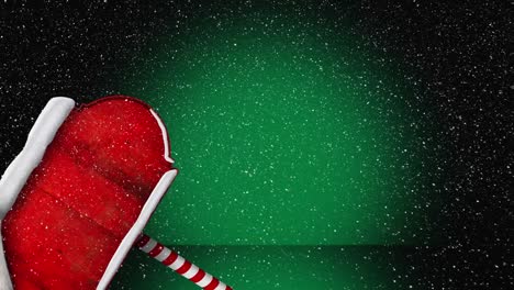 Animation-Von-Schnee,-Der-über-Die-Weihnachtsmütze-Auf-Rotem-Holzschild-Fällt,-Mit-Kopierraum-Auf-Grünem-Hintergrund