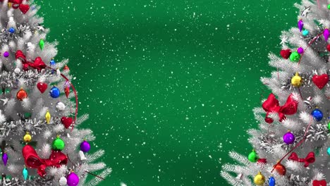 Animation-of-snow-falling-over-two-christmas-trees-with-copy-space-on-green-background