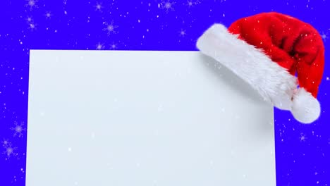Animation-of-santa-hat-and-white-card-with-copy-space-over-snow-falling-on-blue-background
