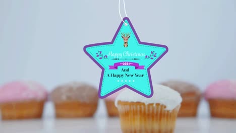 Animation-of-christmas-greetings-on-tag-over-cupcakes-on-white-background