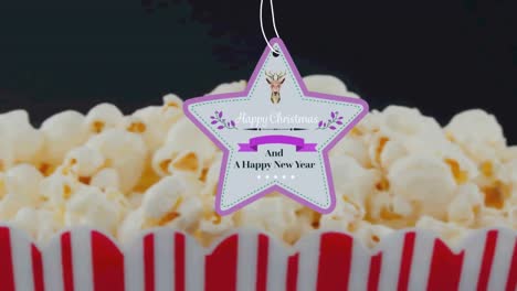 Animation-of-christmas-greetings-on-tag-over-popcorn-on-black-background