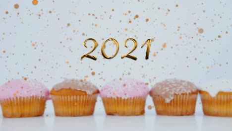 Animation-of-2021-over-cupcakes-on-white-background