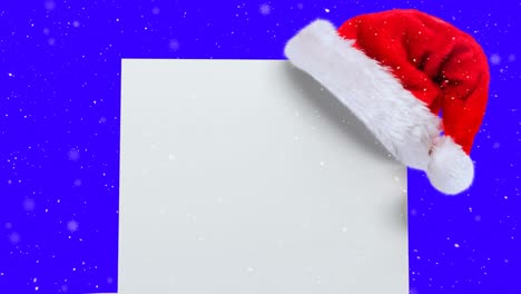 Animation-Von-Weihnachtsmütze-Und-Weißer-Karte-Mit-Kopierraum-über-Schnee,-Der-Auf-Blauen-Hintergrund-Fällt
