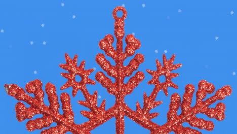 Animation-of-snow-falling-over-red-star-christmas-decoration-on-blue-background