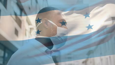 Animation-of-flag-of-honduras-waving-over-man-wearing-face-mask-during-covid-19-pandemic