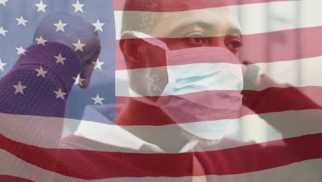 Animation-of-flag-of-usa-waving-over-african-american-man-wearing-face-mask-in-city-street