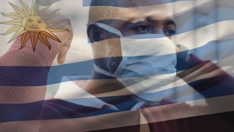 Animation-of-flag-of-uruguay-waving-over-man-wearing-face-mask-during-covid-19-pandemic