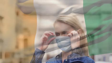 Animation-of-flag-of-ivory-coast-waving-over-caucasian-woman-wearing-face-mask-in-city-street