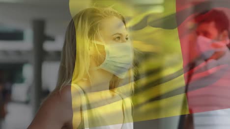 Animation-of-flag-of-belgium-waving-over-woman-wearing-face-mask-during-covid-19-pandemic