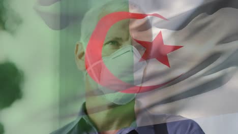 Animation-of-flag-of-algeria-waving-over-caucasian-man-wearing-face-mask-in-city-street