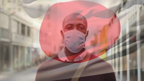 Animation-of-flag-of-japan-waving-over-man-wearing-face-mask-during-covid-19-pandemic