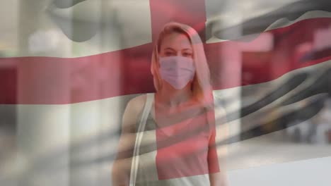 Animation-of-flag-of-england-waving-over-woman-wearing-face-mask-during-covid-19-pandemic