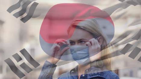 Animation-of-flag-of-korea-waving-over-woman-wearing-face-mask-during-covid-19-pandemic
