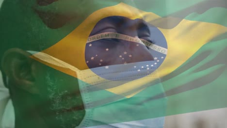Animation-of-flag-of-brazil-waving-over-african-american-man-wearing-face-mask