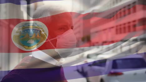 Animation-of-flag-of-costa-rica-waving-over-caucasian-man-wearing-face-mask-in-city-street